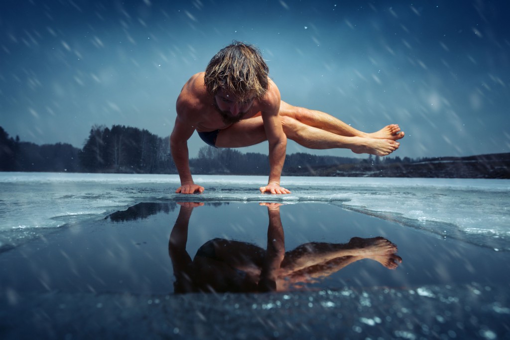 Man doing yoga exercise (parsva bakasana) on the ice of frozen lake at winter snowy day