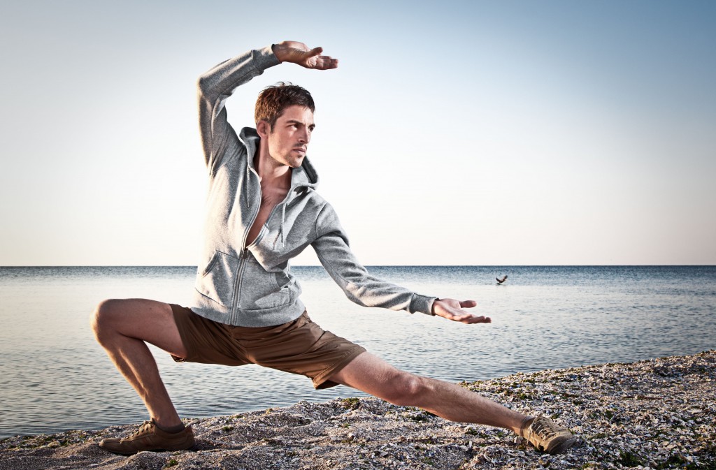 Young attractive man making Thai-chi movements on the beach of Black sea
